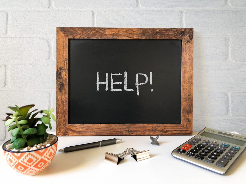 Chalkboard with "Help!" written on it with plants, pen, binder clips, and calculator near.